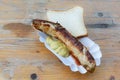 Roasted sausage or German bratwurst on a paper plate with mustard and bread on an old wooden table, typical outdoor fast food on a Royalty Free Stock Photo