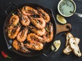 Roasted tiger prawns in iron grilling pan with fresh leek, lemon, bread and pesto sauce over black background Royalty Free Stock Photo