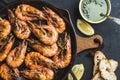 Roasted tiger prawns in iron grilling pan with fresh leek, lemon slices, bread and pesto sauce over black background Royalty Free Stock Photo
