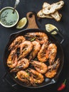 Roasted tiger prawns in iron grilling pan on wooden board with fresh leek, lemon slices, pepper, bread and pesto sauce Royalty Free Stock Photo