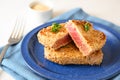 Roasted tuna steak in sesame seeds with parsley garnish on a blue plate on a white table, selected focus, narrow depth of field Royalty Free Stock Photo