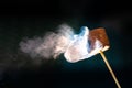 Roasting chocolate coated marshmallow on a stick; smoke swirls visible on a dark background Royalty Free Stock Photo