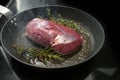 Roasting a raw duck breast on the skin side in steaming oil with thyme and rosemary in a frying pan on a black stove, cooking Royalty Free Stock Photo