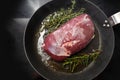 Roasting a raw duck breast with thyme and rosemary in a frying pan on a black stove, cooking concept, copy space, high angel view Royalty Free Stock Photo