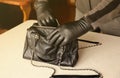 Robber in black outfit and gloves see on opened stolen women bag. A thief evaluates the value of stolen items from a