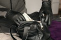 Robber in black outfit and gloves see in opened stolen women bag. The thief takes out US dollar bills from a womans handbag in Royalty Free Stock Photo