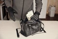 Robber in black outfit and gloves see in opened stolen women bag. The thief takes out US dollar bills from a womans handbag in Royalty Free Stock Photo