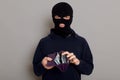 A robber thief man with a disguised face holds an open stolen wallet with money in his hands, looks at the camera, is dressed in a