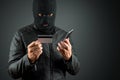 Robber, a thug in a balaclava holds a credit card in his hands on a dark background. Robbery, hacker, crime, theft. Copy space Royalty Free Stock Photo