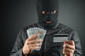 Robber, a thug in a balaclava holds a credit card in his hands on a dark background. Robbery, hacker, crime, theft. Copy space