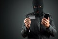 Robber, a thug in a balaclava holds a credit card in his hands on a dark background. Robbery, hacker, crime, theft. Copy space Royalty Free Stock Photo