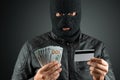 Robber, a thug in a balaclava holds a credit card in his hands on a dark background. Robbery, hacker, crime, theft. Copy space