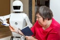 Robot friend is learning or teaching with an disabled woman, reaching her a pencil