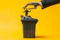 Robot hand throwing a businessman into a garbage can, over yellow background