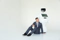 Businessman uses a smartphone while sitting on the floor next to a robot. Modern Robotic Technologies. Humanoid Royalty Free Stock Photo