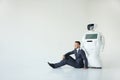 Businessman uses a smartphone while sitting on the floor next to a robot. Modern Robotic Technologies. Humanoid Royalty Free Stock Photo