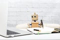 Robot sits at the table and holds a pen in his hand
