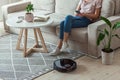 Robot vacuum cleaner cleaning carpet, woman remote control mobile phone and enjoy rest, sitting on sofa home Royalty Free Stock Photo