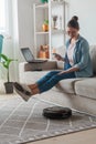 Robotic vacuum cleaner cleaning carpet, woman remote control mobile phone and enjoy rest, sitting on sofa home Royalty Free Stock Photo