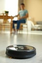 Robotic vacuum cleaner cleaning floor while man relaxing at home, selective focus Royalty Free Stock Photo