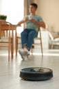 Robotic vacuum cleaner cleaning floor while man relaxing at home, selective focus Royalty Free Stock Photo