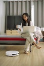 Robotic vacuum cleaner cleaning the room while woman working with laptop computer on sofa at home