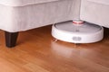 Robotic vacuum cleaner runs under sofa in room on laminate floor modern smart cleaning technology housekeeping Royalty Free Stock Photo