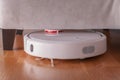 Robotic vacuum cleaner runs under sofa in room on laminate floor. Robot controlled by voice commands to direct cleaning. Modern sm Royalty Free Stock Photo