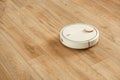 Robotic vacuum cleaner working on laminate wood floor in the living room. Automated white vacuum cleaner robot. Copy space for a Royalty Free Stock Photo