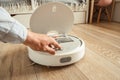 Robotic vacuum cleaner working on laminate wood floor in the living room. Man switching on automated white vacuum cleaner robot Royalty Free Stock Photo