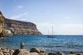 Rock beach with sailboat on blue sea in Puerto de Mogan Royalty Free Stock Photo