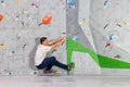 Rock climber man hanging on a bouldering climbing wall, inside on colored hooks