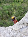 Rock climber rappeling from a gray rock cliff into a lush green forest below