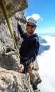 Rock climber on a vertical rock face climbing and smiling above a sea of clouds in the valley below