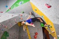 Rock climber woman hanging on a bouldering climbing wall, inside on colored hooks