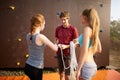 Rock climbing instructor is coaching how to tie knot. Male coach fixing rope into belay. Instructor preparing young