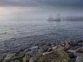 Rock coast line in foreground, ocean and background with town building and ship in fog. Calm nature scene with muted color and Royalty Free Stock Photo