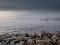 Rock coast line in foreground, ocean and background with town building and ship in fog. Calm nature scene with muted color and Royalty Free Stock Photo