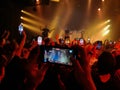 At a rock concert, many audience members film the scene on mobile phones. Red blurred background