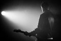 Rock guitarist man in leather jacket standing his back in smoky studio or stage masterfully playing electric guitar Royalty Free Stock Photo