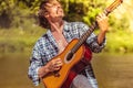 Rock guitarist in an open shirt enthusiastically plays the old guitar in nature