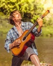 Rock musician man in an open shirt enthusiastically plays the old guitar in nature. Summer, clear day Royalty Free Stock Photo