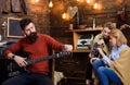 Rock musician with trendy beard and mustache playing guitar. Bearded man tuning musical instrument. Mom and daughter