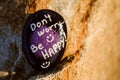 A rock painted black and purple stating Don't worry be happy