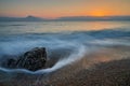 A rock on the pebble beach is hit by the sea wave at sunset Royalty Free Stock Photo