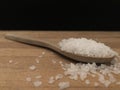 Rock salt in the wooden spoon on the wooden cutting board with black backboard.