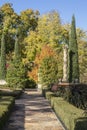 Rock sidewalk through formal garden toward gate with lantern past pillar and tall trees in early autumn Royalty Free Stock Photo