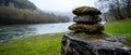 A rock stack with moss on top sits in a grassy area next to a river. Royalty Free Stock Photo