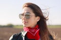 Rock style. Close up shot of dark haired thoughtful woman dressed in leather jacket, red bandana and sunglasses, focused into dist