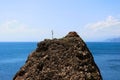 A rock texture of a mountainous rock on which a dried lone plant against the blue sea and sky. The peak of the mountain above sea Royalty Free Stock Photo